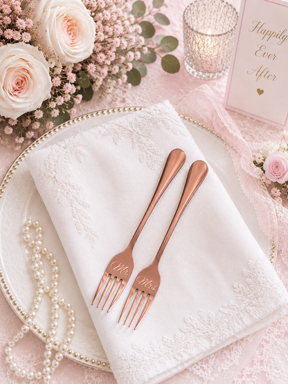 Rose gold 'Mr.' and 'Mrs.' forks on a white napkin with floral and pearl decorations.