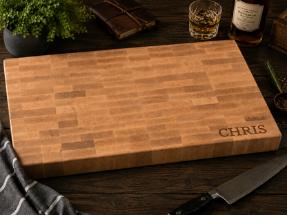 Wooden cutting board with 'CHRIS' engraving on a wooden surface with a knife and glass.