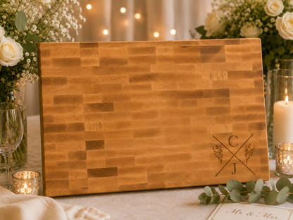 Wooden cutting board with initials on a decorative table setting with flowers and candles.